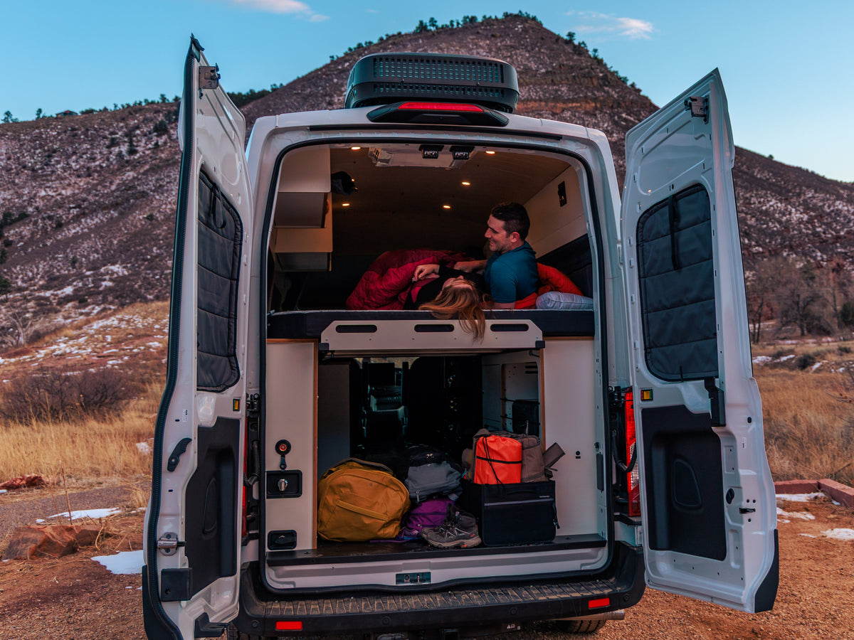 People loading hiking gear into the back of a camper van