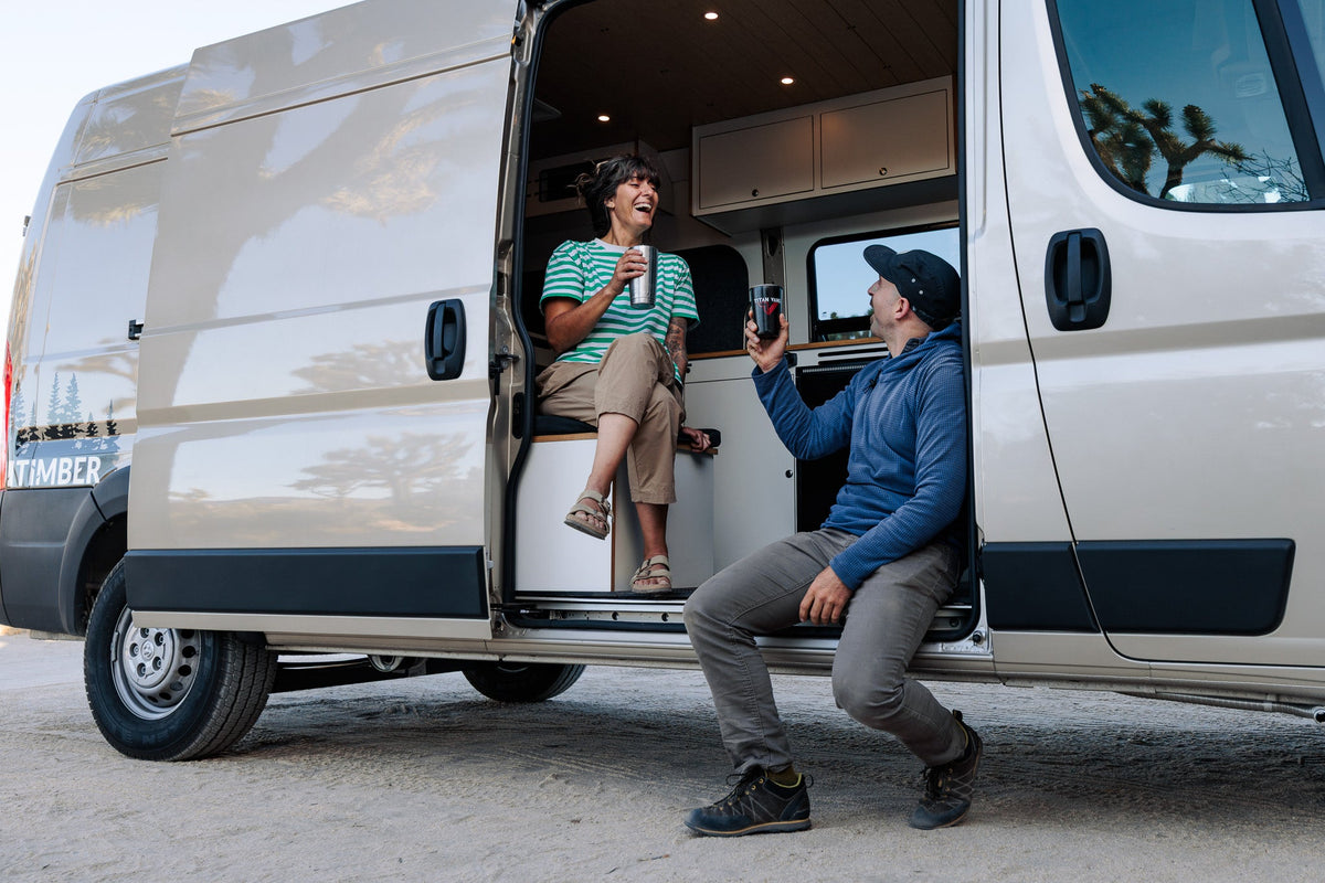 Two people sitting in the open sliding door of a camper van