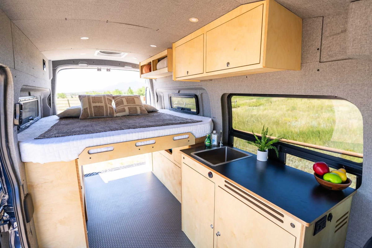 Timber camper van interior showing the galley, bed and overhead cabinetry